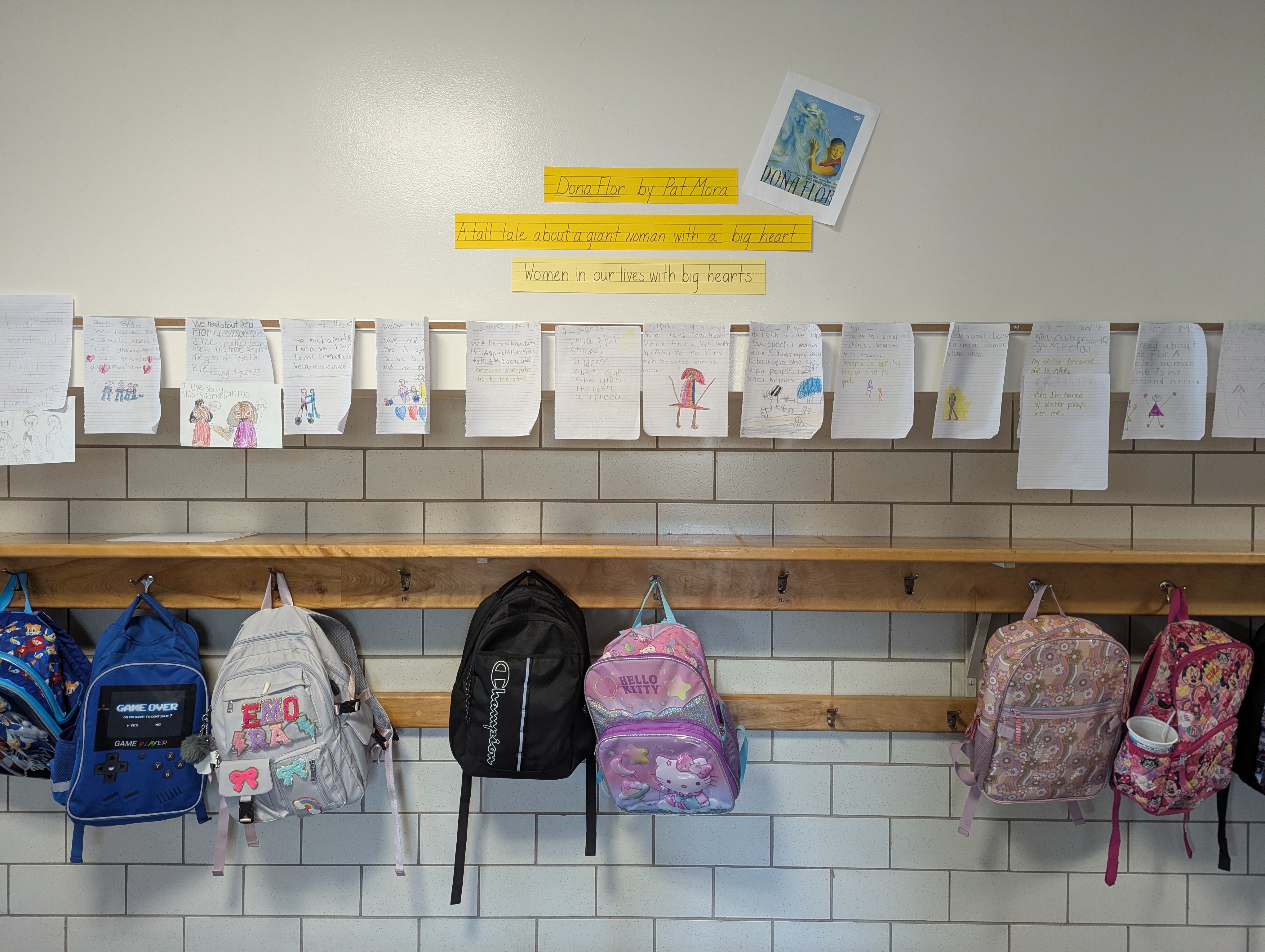Student art hanging on the wall above backpacks hanging on their hooks