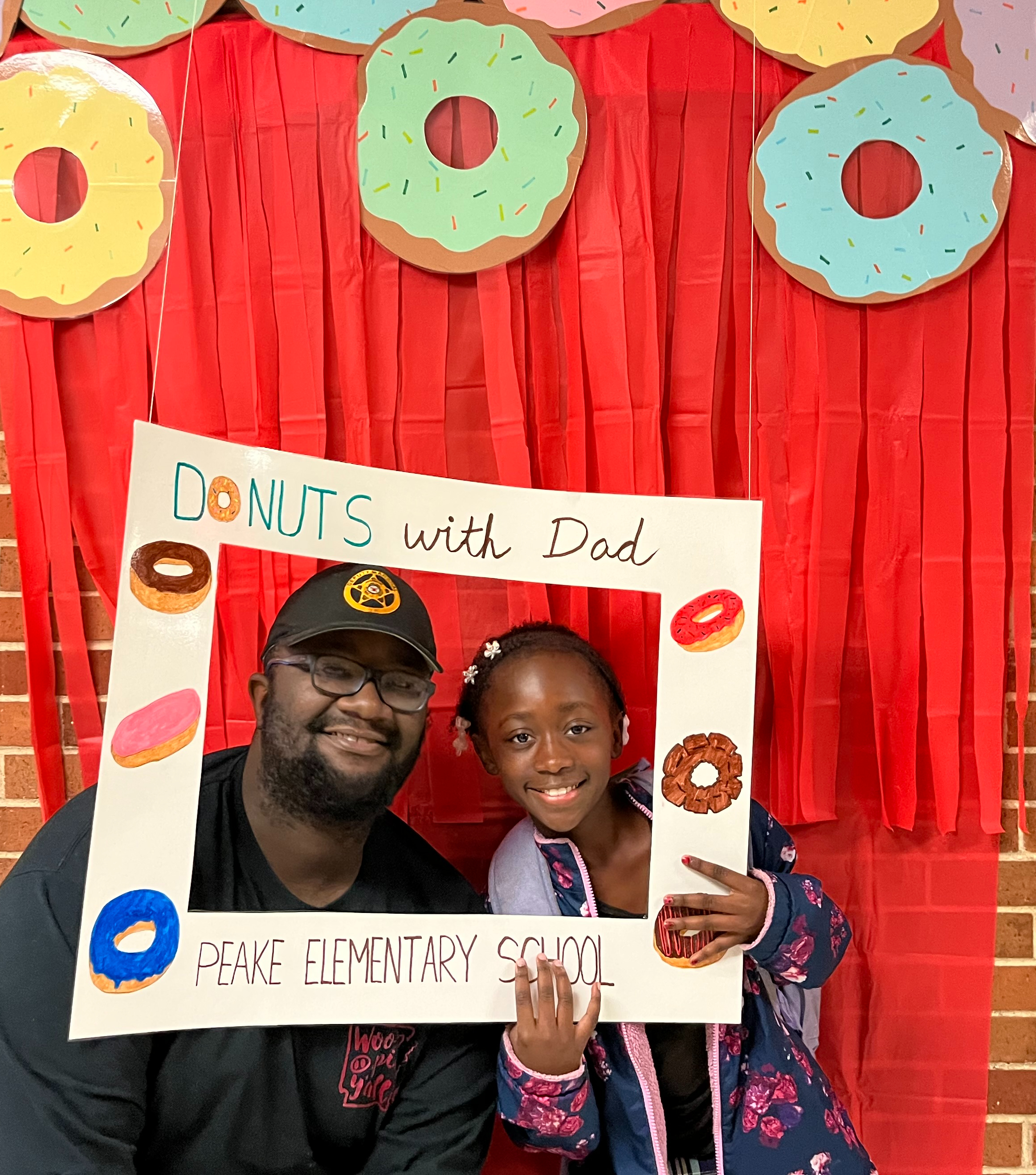 child and dad smiling in a picture frame that says "donuts with Dads"