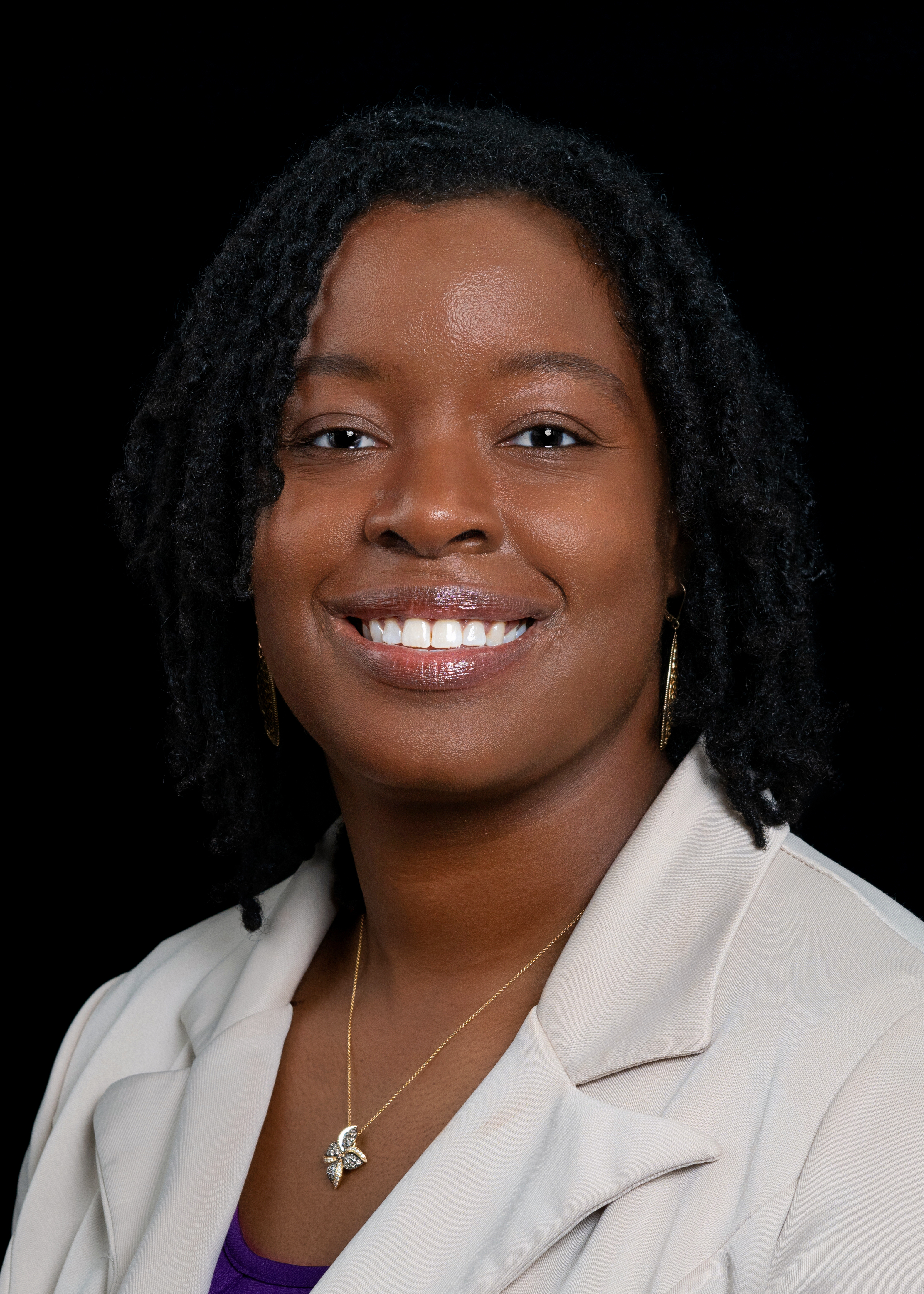 brown skin woman smiling with black locs tan blazer and gold star necklace