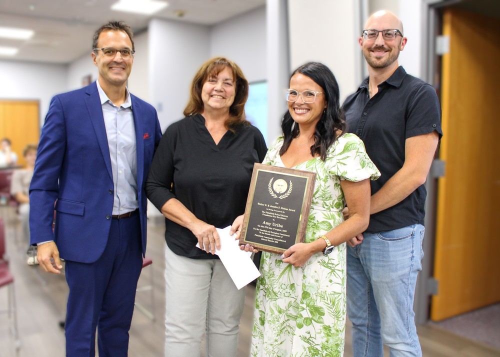 four people stand. one holds awards plaque