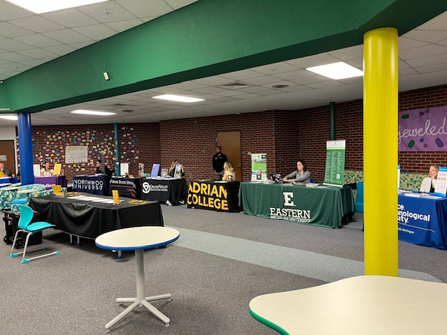 college representatives at tables with college names: Adrian College, Eastern Michigan University