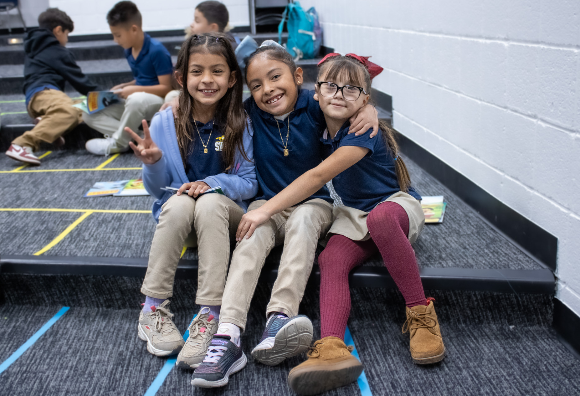 Three students hug while seated on the auditorium's stair. 