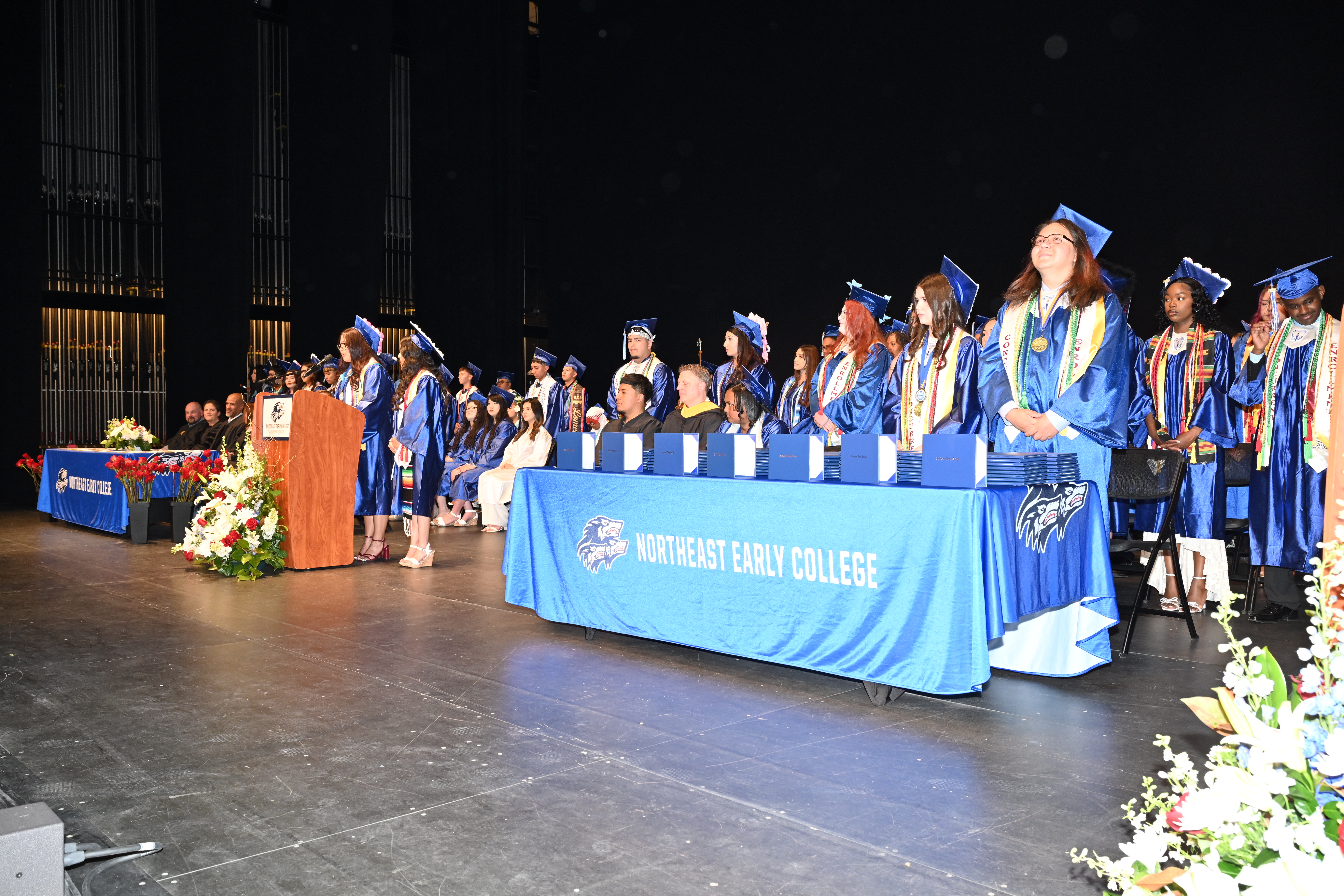 Stage full of NEC graduates in their caps and gowns.