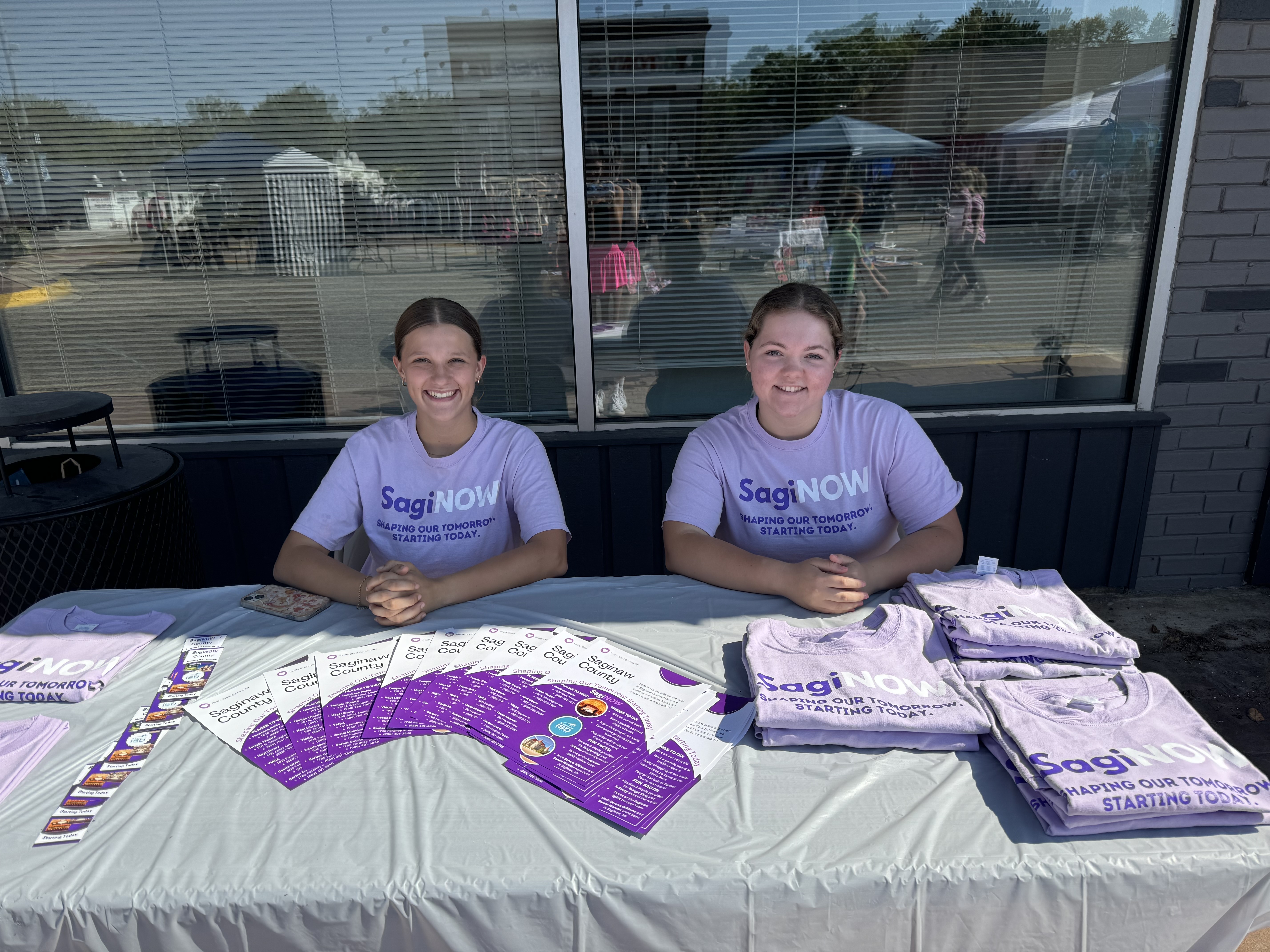 two student ambassadors at a table with purple tshirts handing out brochures and swag