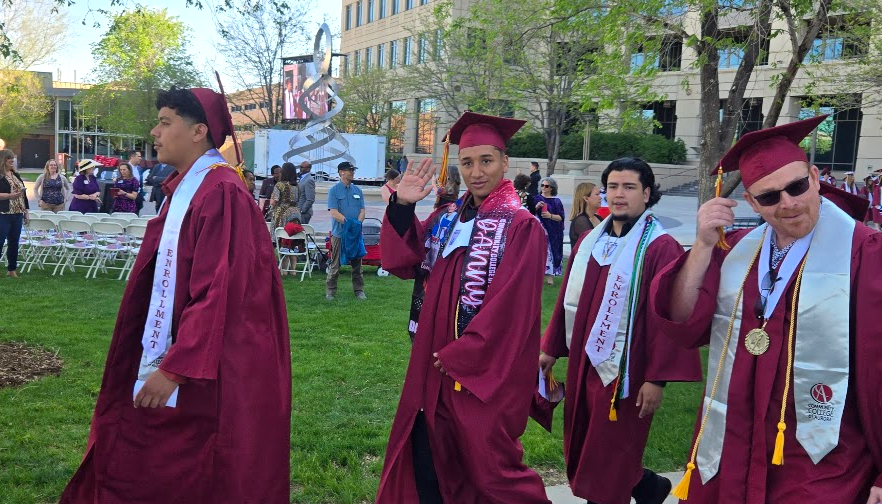 CCA graduates walking on the lawns in their caps and gowns. One student waves at the camera.