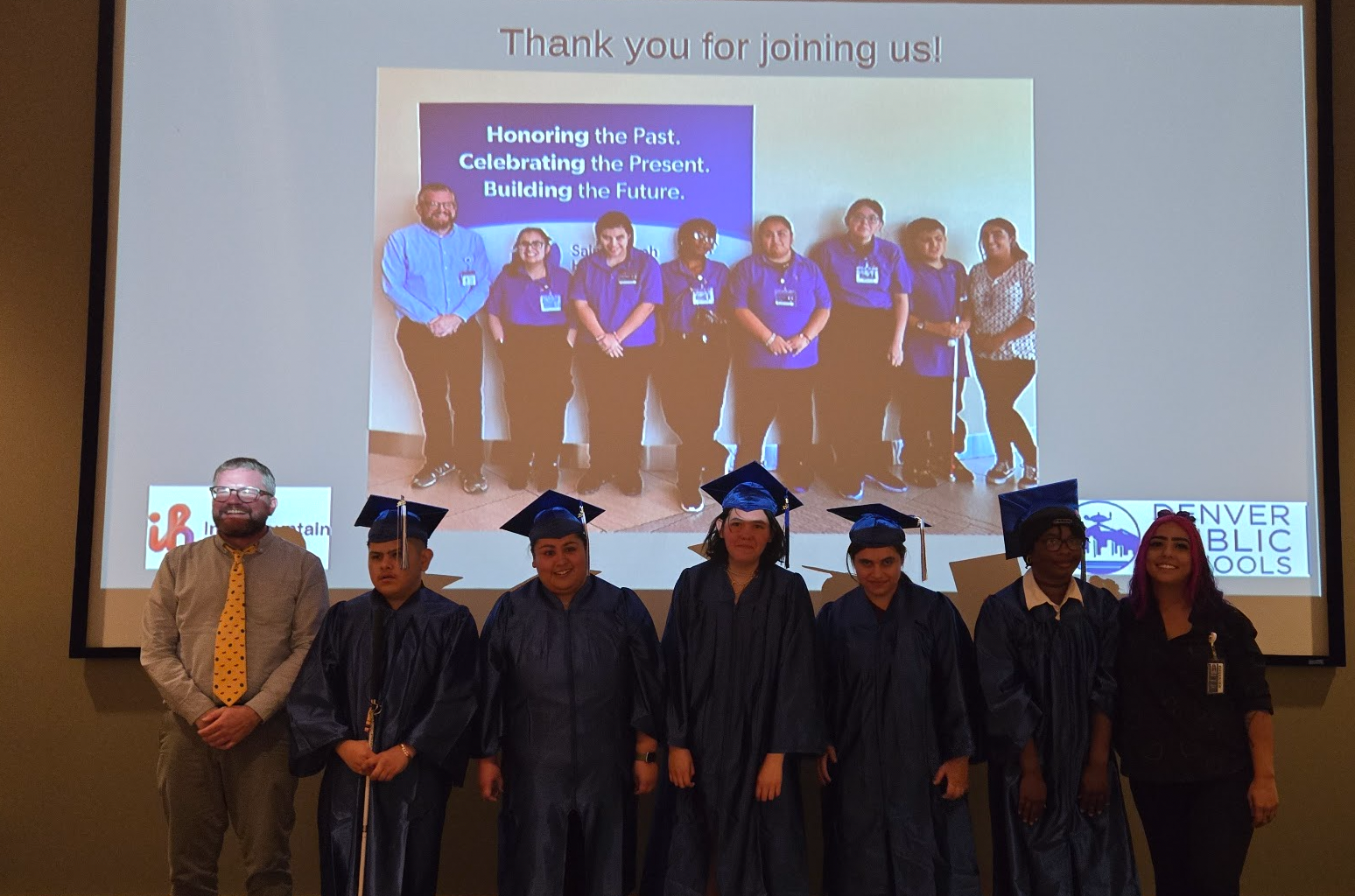 6 students in caps and gowns and 2 adults facing the camera
