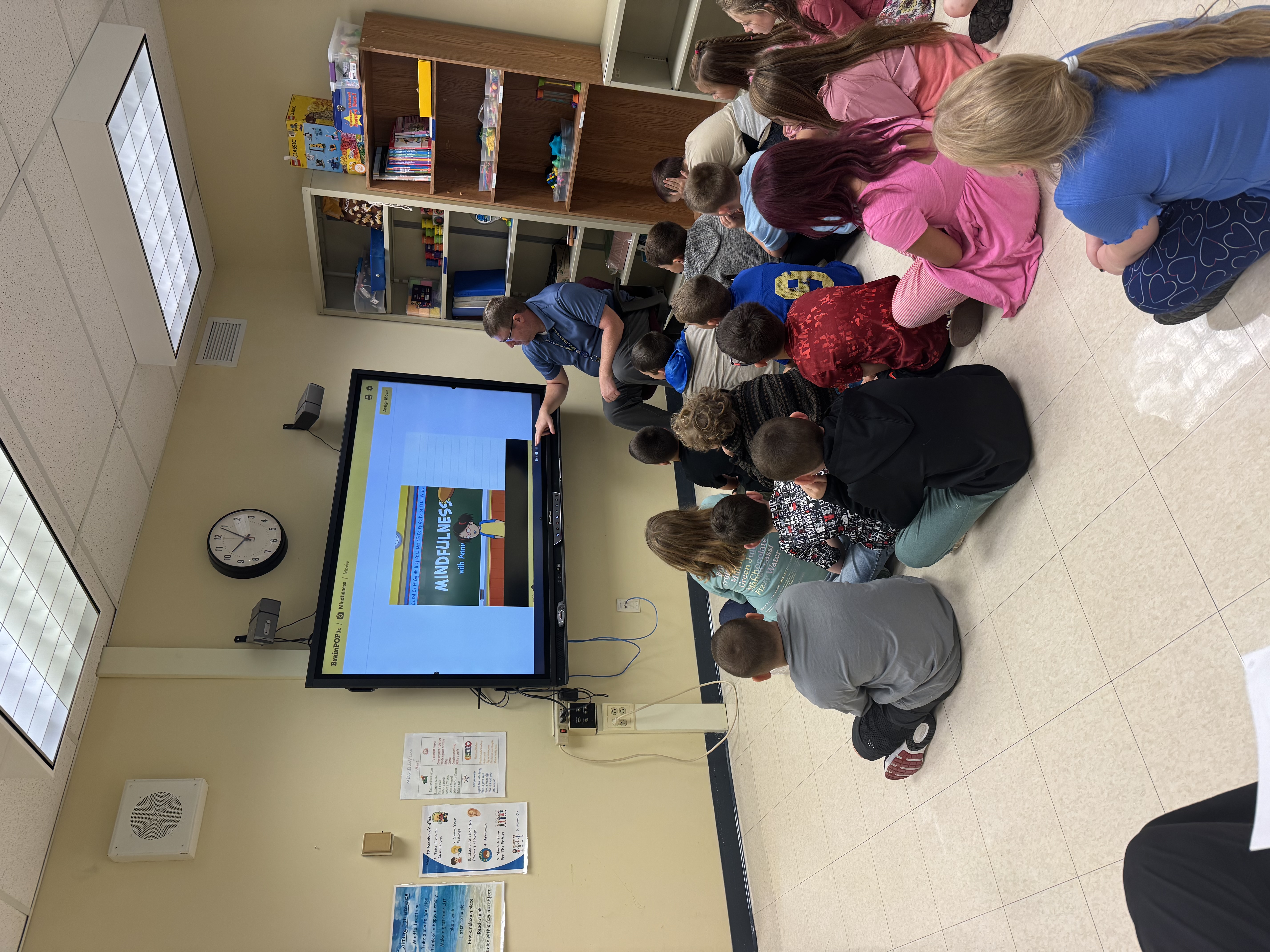 a picture of students sitting on the floor looking at a video about mindfulness