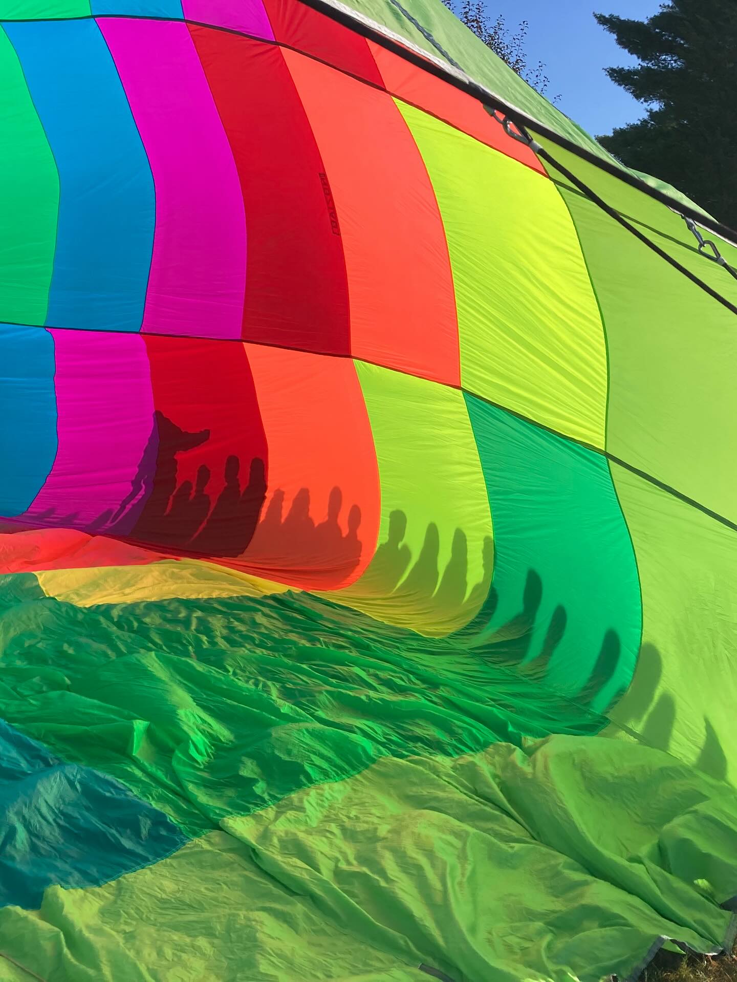 A picture of the inside of an inflating multi colored hot air balloon with shadows of children on the outside