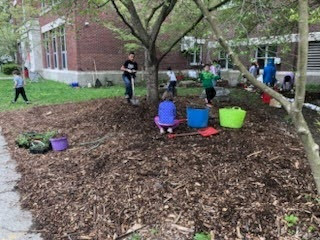 BJM students outside the school building spreading mulch and cleaning up the garden beds. 