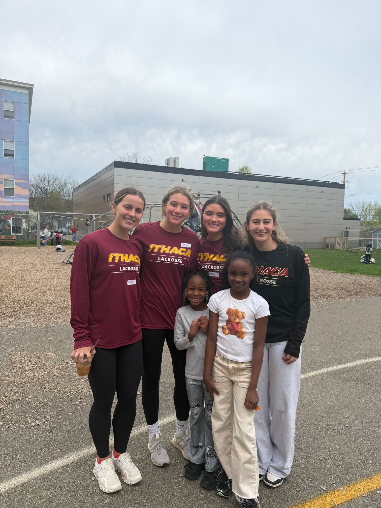Ithaca High School girls in Ithaca Athletics tshirts stand with two BJM students outside. 