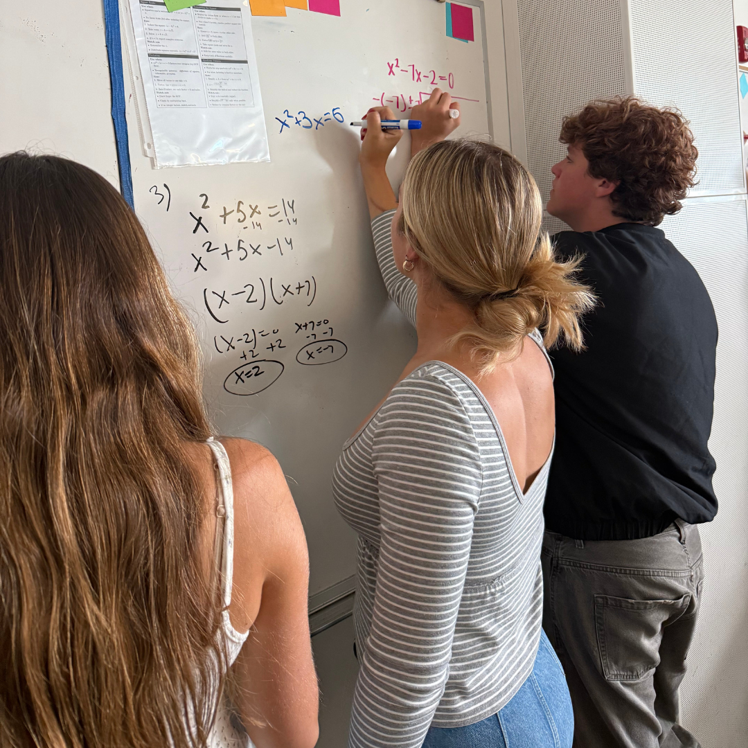 Three MCHS students solving math problems at whiteboard.