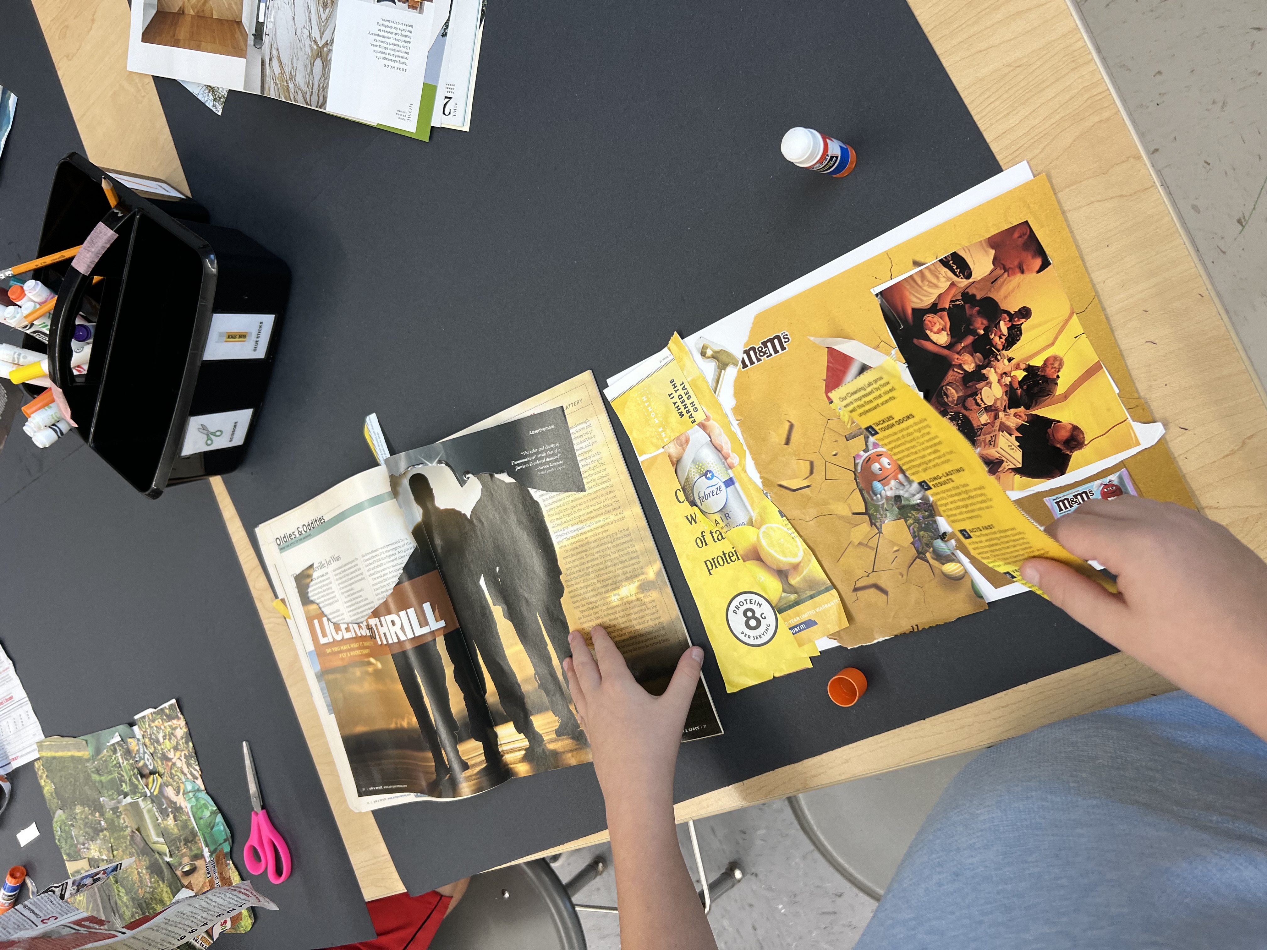 A person sits at a table, working on an art project. The table has scissors, glue, and papers.