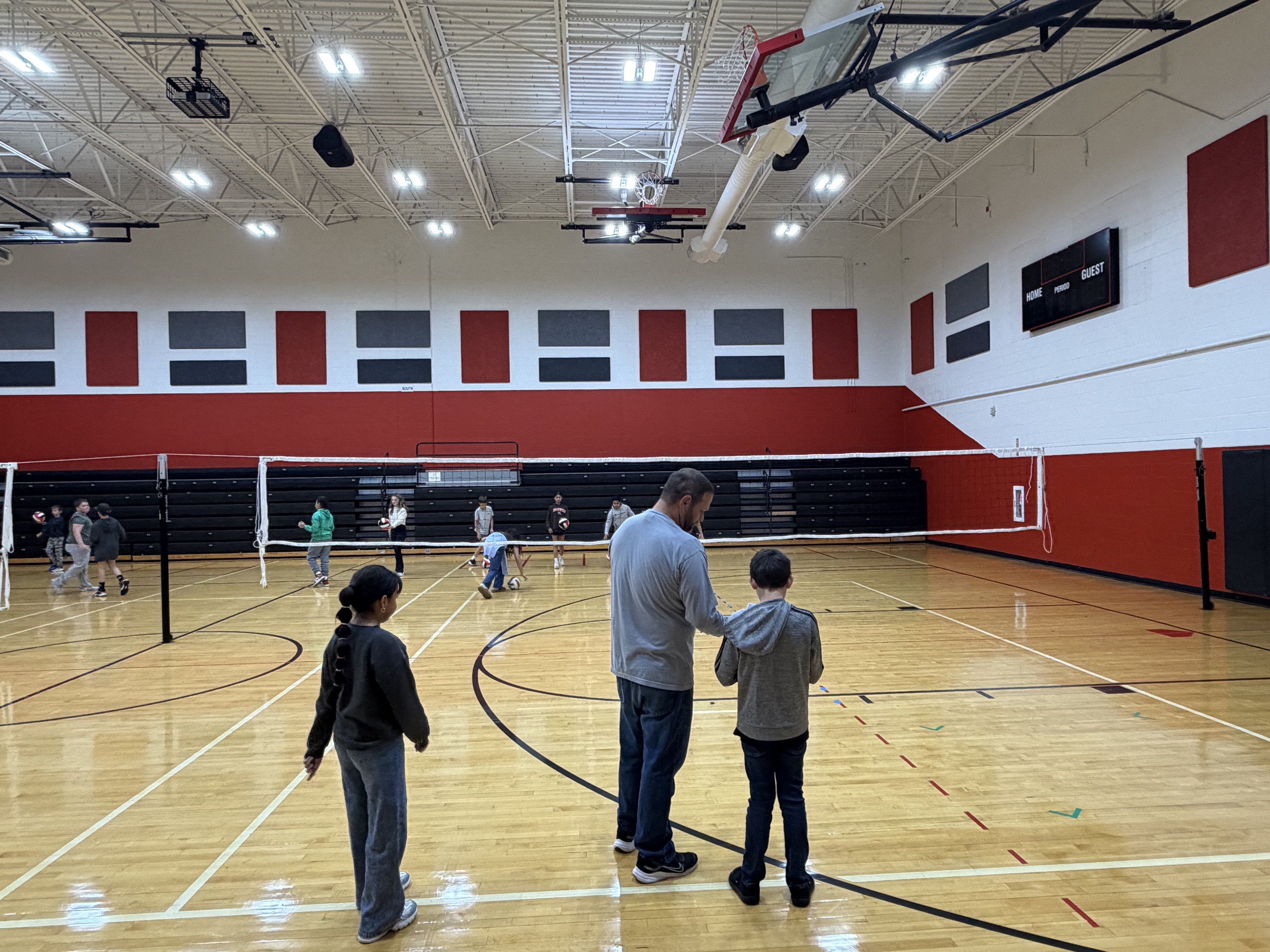 People stand in an indoor basketball court. A net is in the middle of the court.