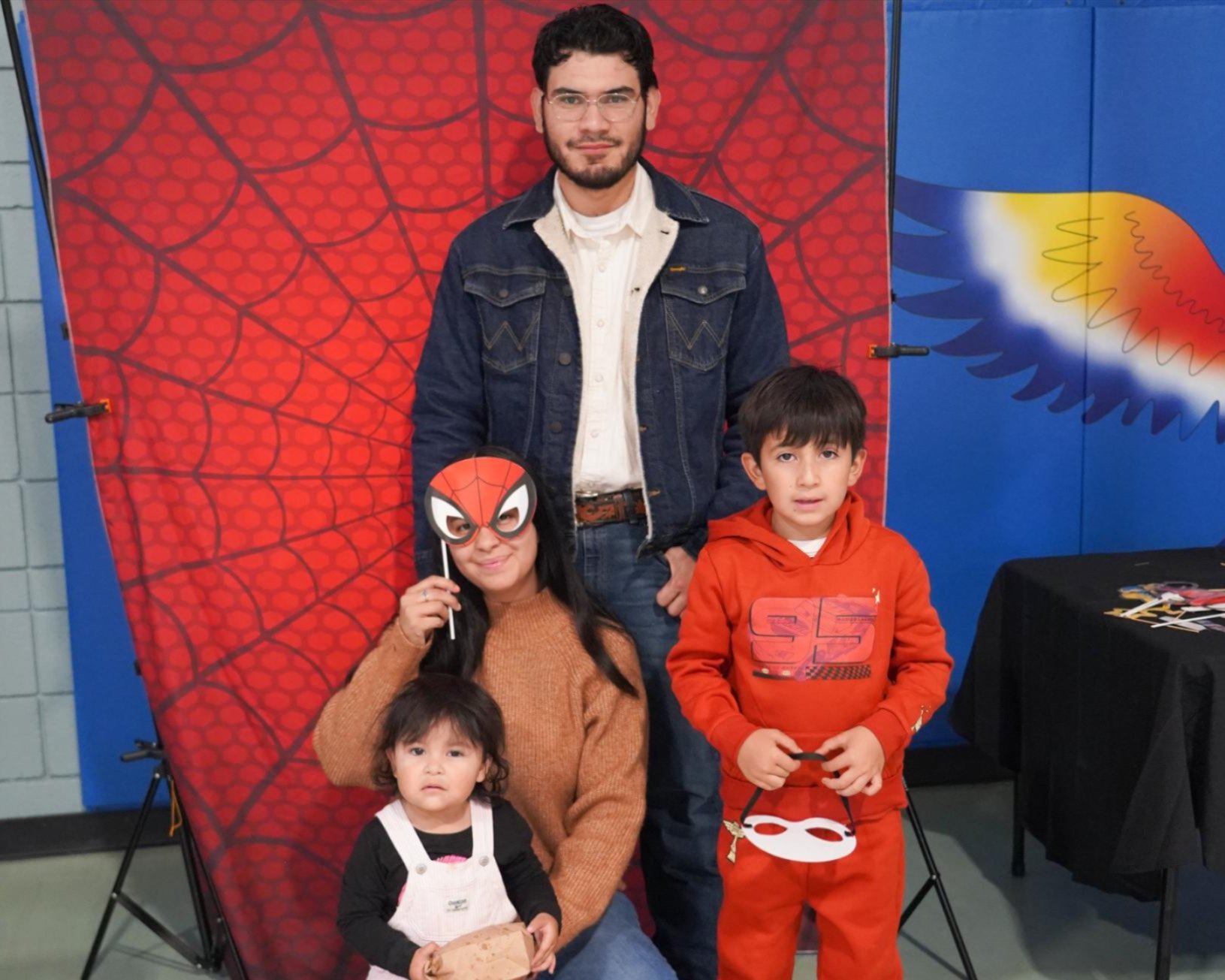 Family with two children in costumes posing in front of a backdrop. A child wearing a Spider-Man mask.