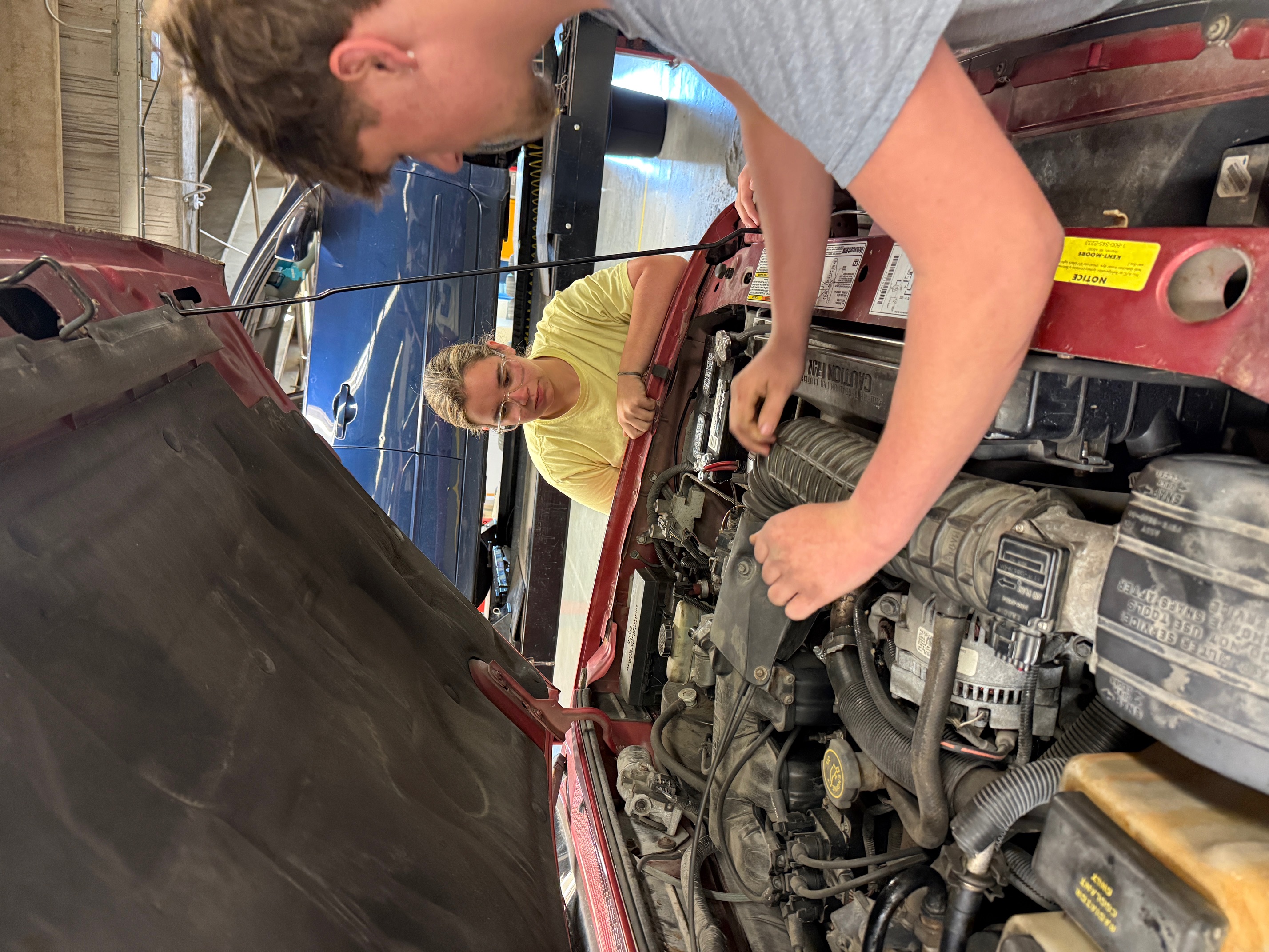 Students work in a hood of a car