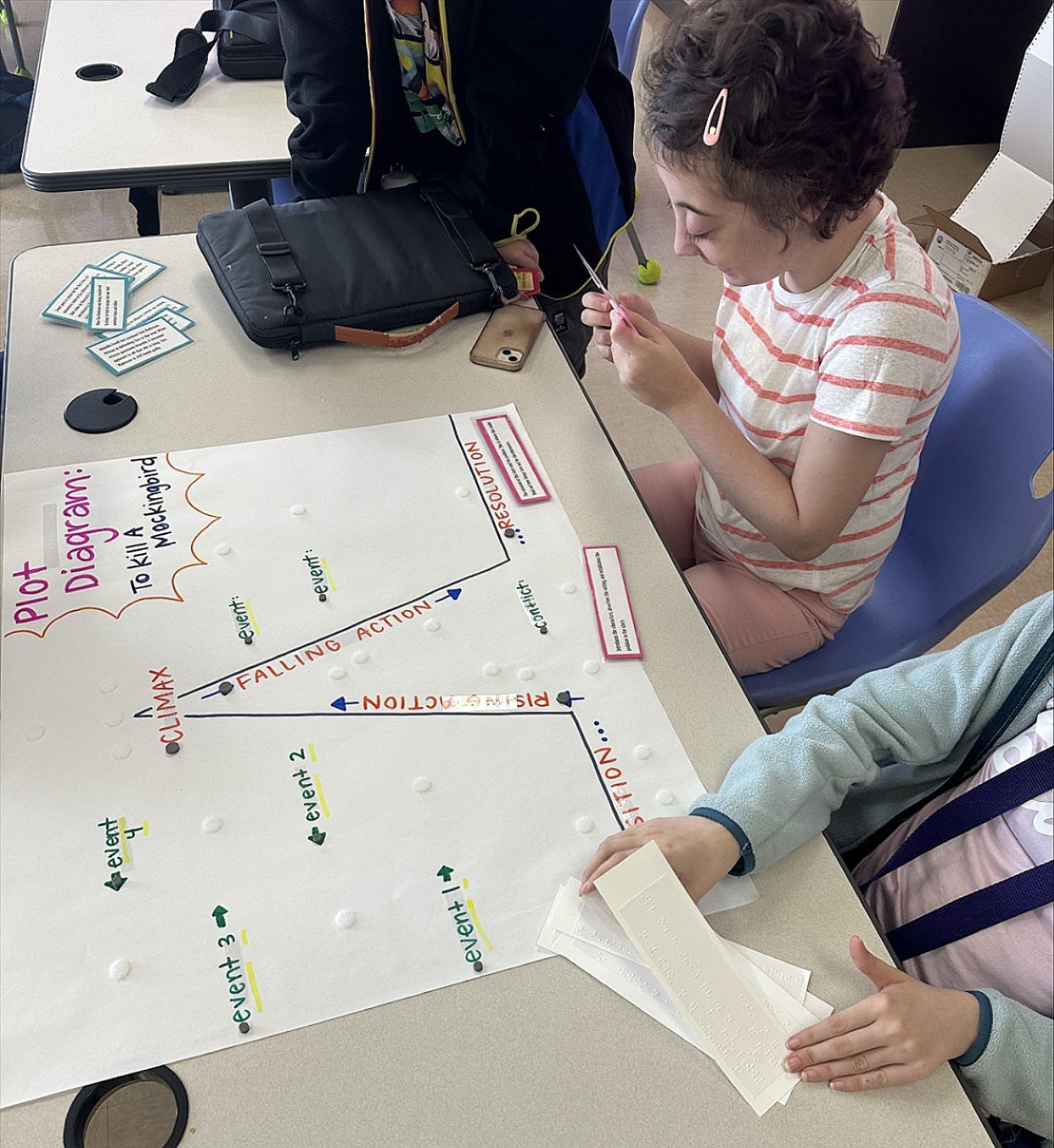 Danika and a classmate reading their choices and gluing them onto their poster board