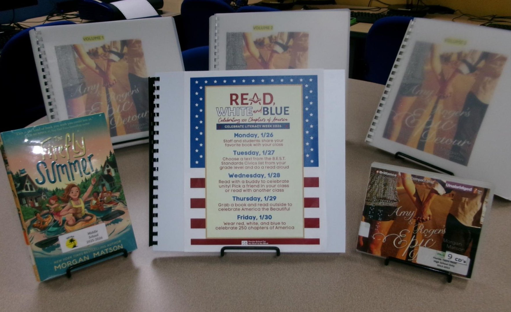 The Read, White, and Blue Celebrate Literacy event flyer is center of the table; it is surrounded by a variety of books that closely match the theme