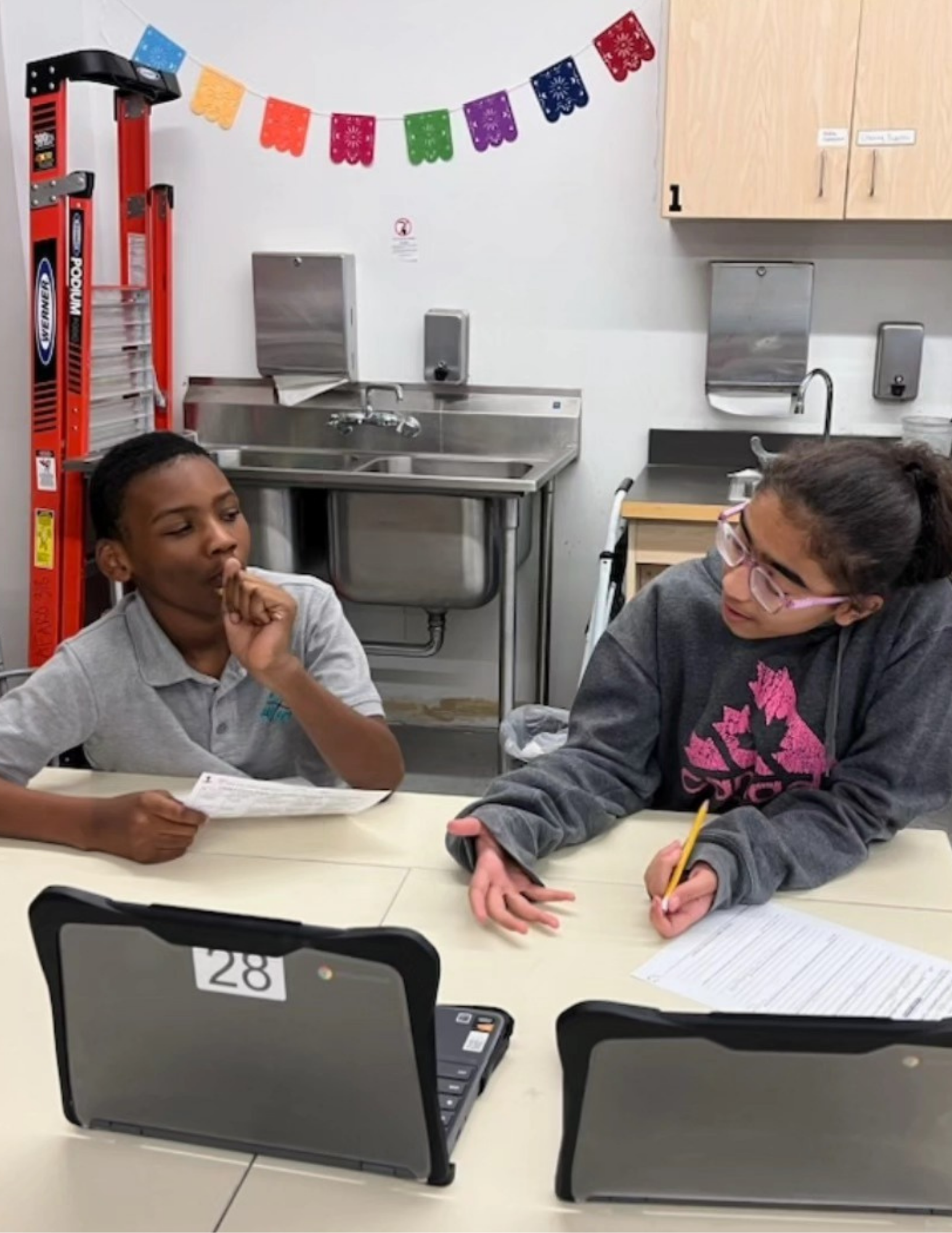 Dos estudiantes discutiendo sobre las tareas escolares, sentados frente a sus computadoras portátiles