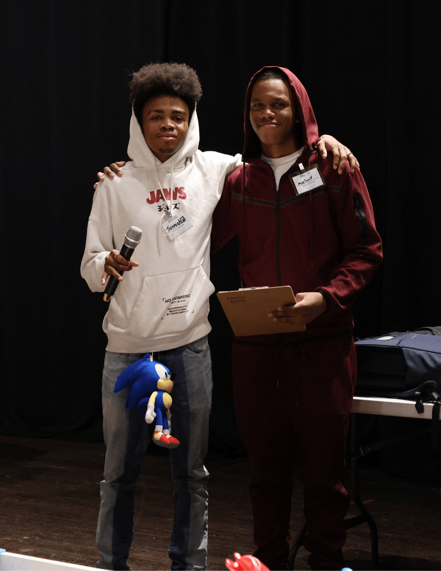 2 estudiantes: uno está sosteniendo un micrófono y el otro está sosteniendo una carpeta