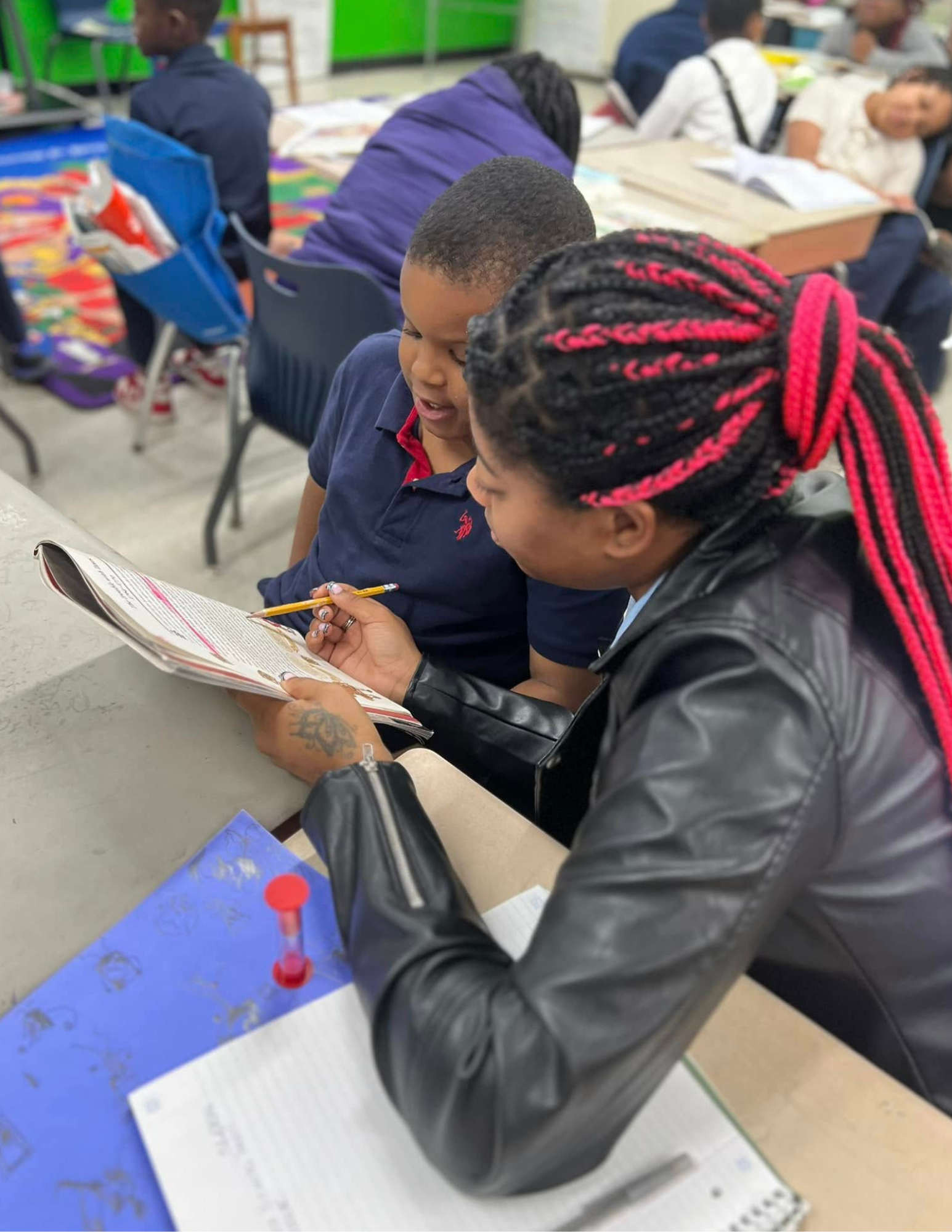 Una estudiante mayor le enseña a uno más joven algunos papeles en una carpeta.