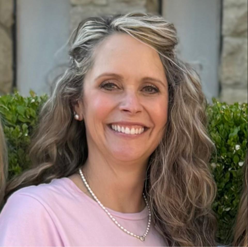 picture of woman with curly brown hair wearing a pink shirt and pearls