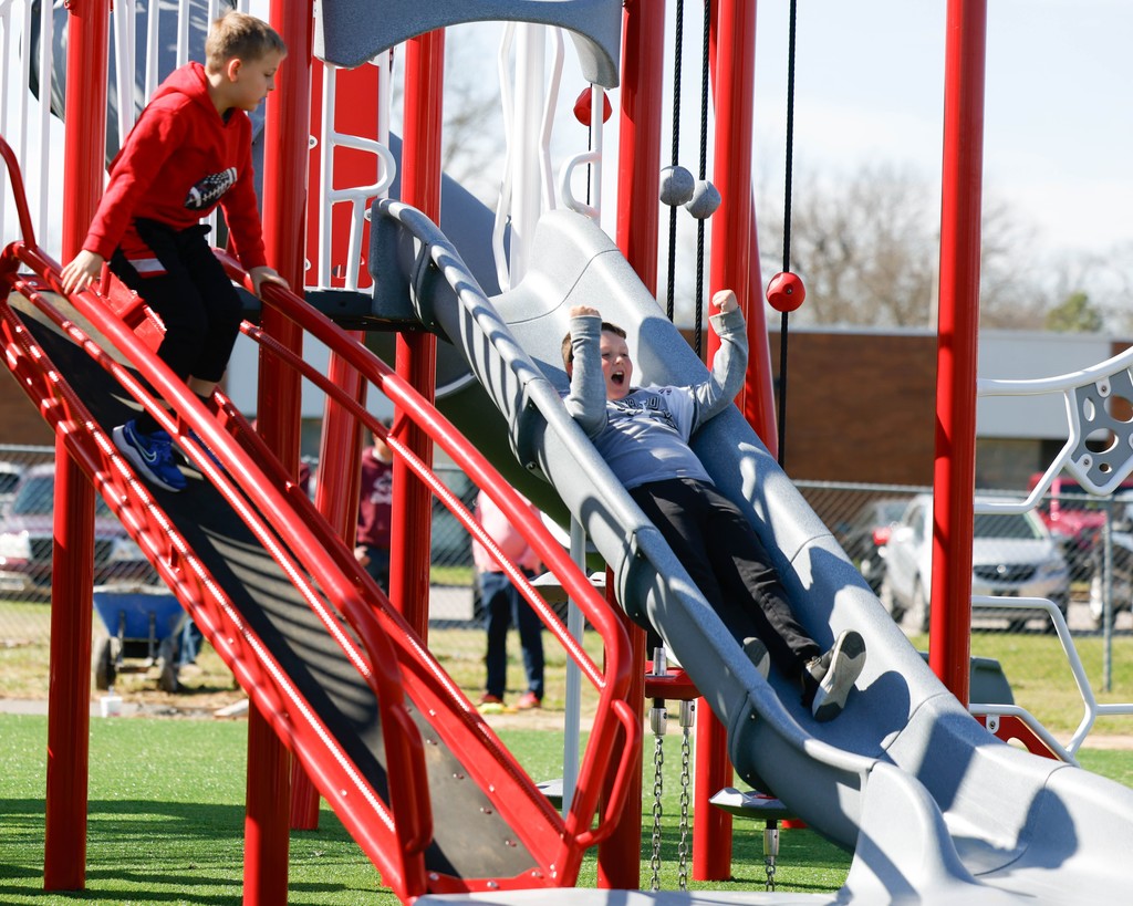 child sliding down a playset slide with another boy beside him