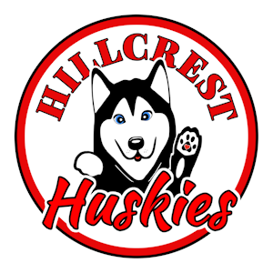 A circular Hillcrest Huskies logo is displayed on a transparent background. The logo features a white circle bordered by a thick red ring with a thin black outline. Curving across the top of the circle, large red capital letters outlined in black spell “HILLCREST.” Centered within the logo is a friendly cartoon husky with black-and-white fur, bright blue eyes, a black nose, and an open mouth showing a small pink tongue. The husky is facing forward with one front paw raised in a waving gesture. The raised paw includes black paw pads with a small red paw pad in the center. Across the bottom of the logo, the word “Huskies” appears in large red script outlined in black, partially overlapping the husky illustration. The logo uses red, black, white, blue, and pink accents and serves as the official Hillcrest Elementary Huskies mascot emblem.