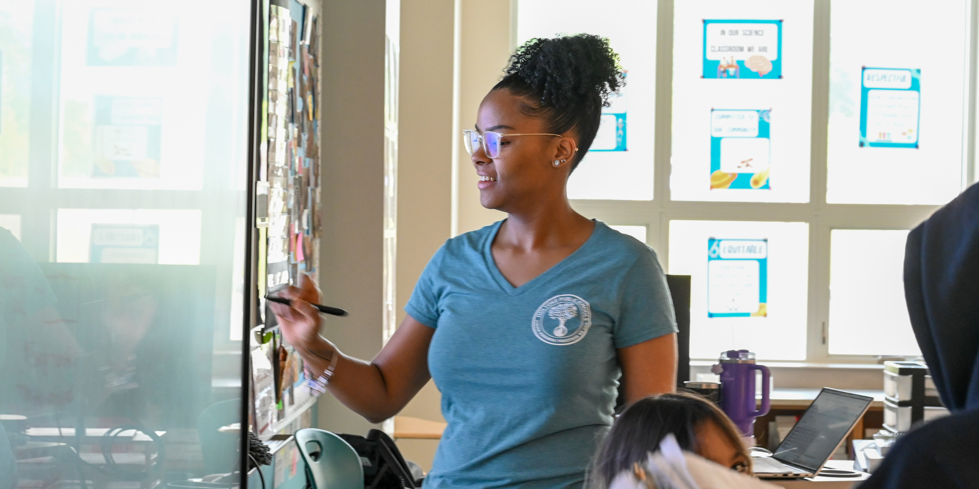A teacher writes on a smart board in front of her class