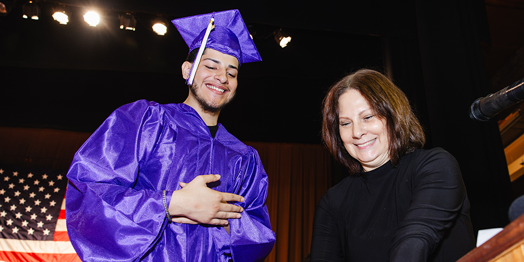 Student wearing graduation cap and gown with staff member 