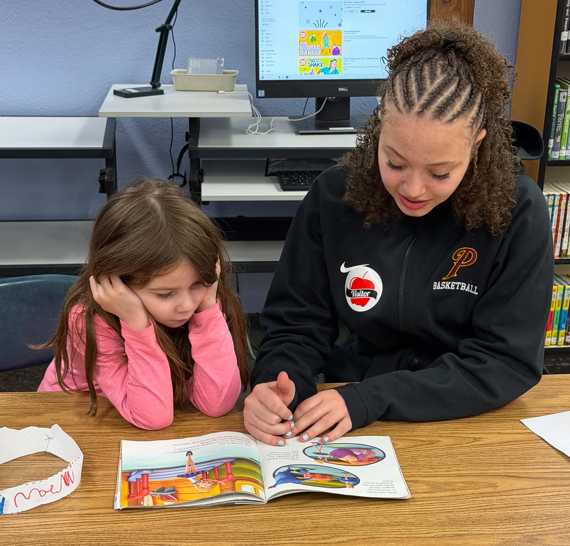 A high schooler reads to a primary school student.