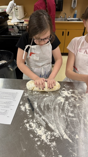 Students pose with rolling pins while wearing aprons and toques