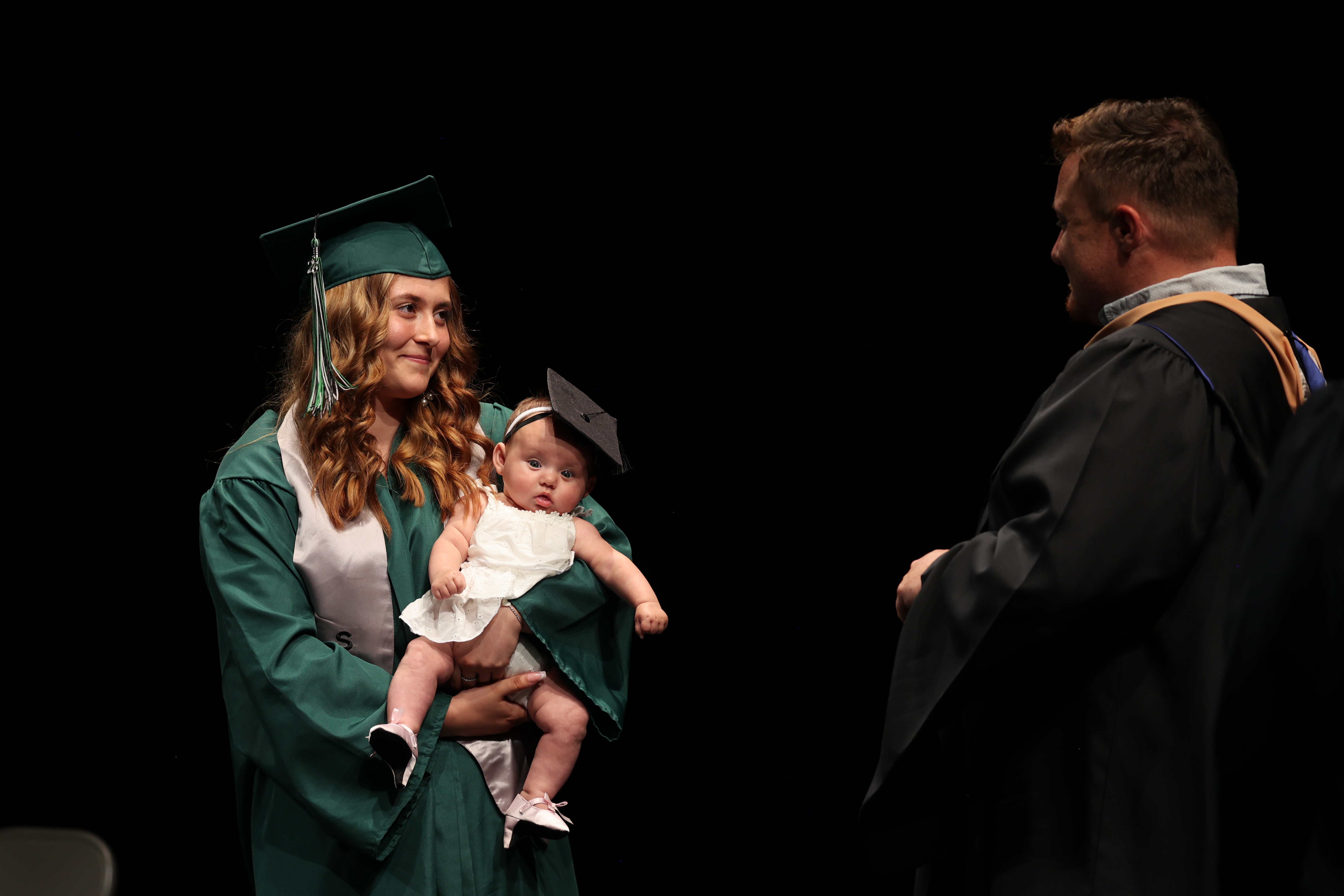 A Summit View High School graduate holding her child prepares to accept her diploma.