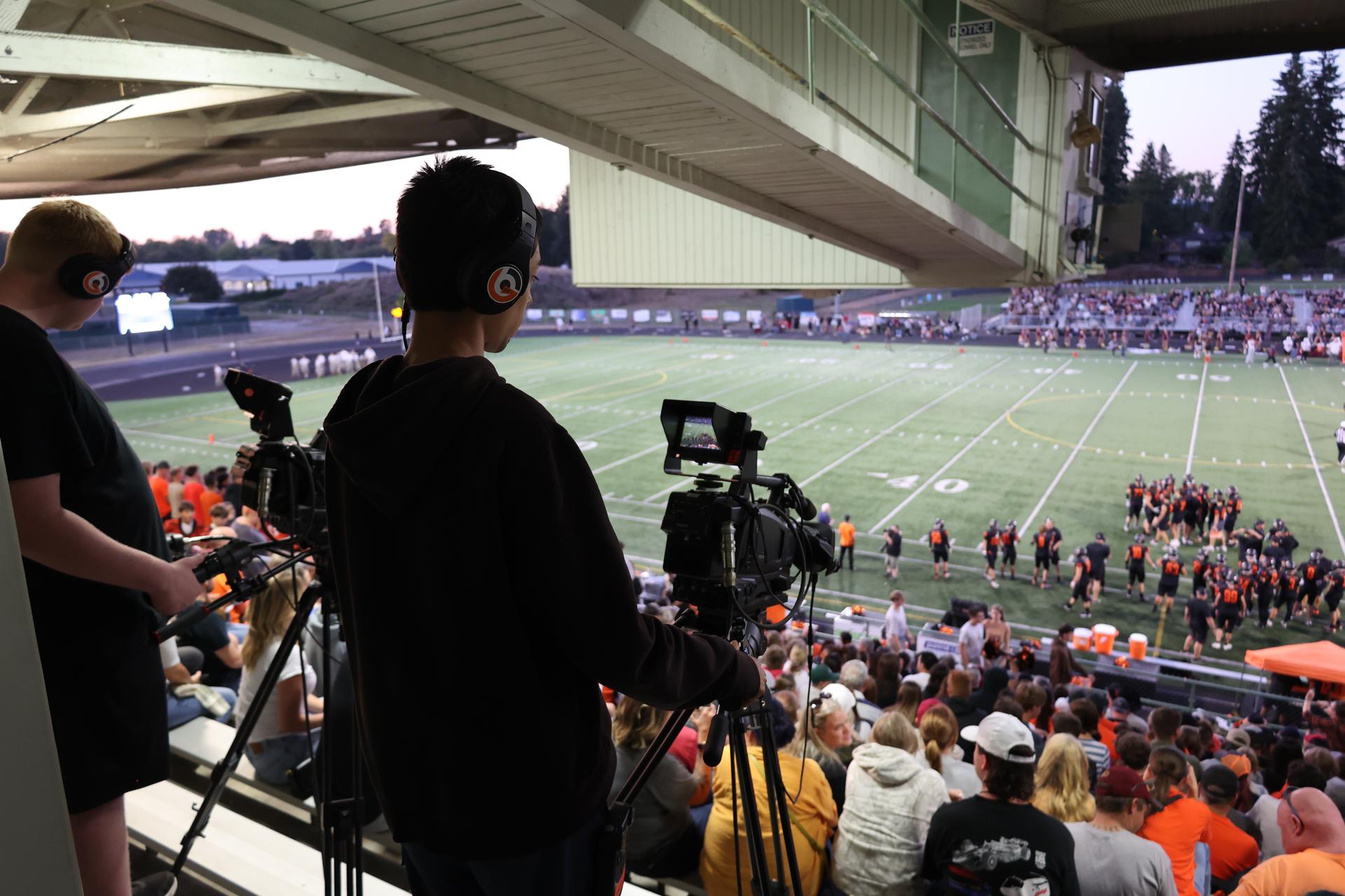 Two video production students film a football game