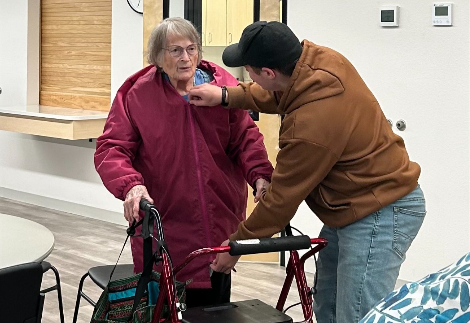 A student helps a senior citizen zip up her coat.