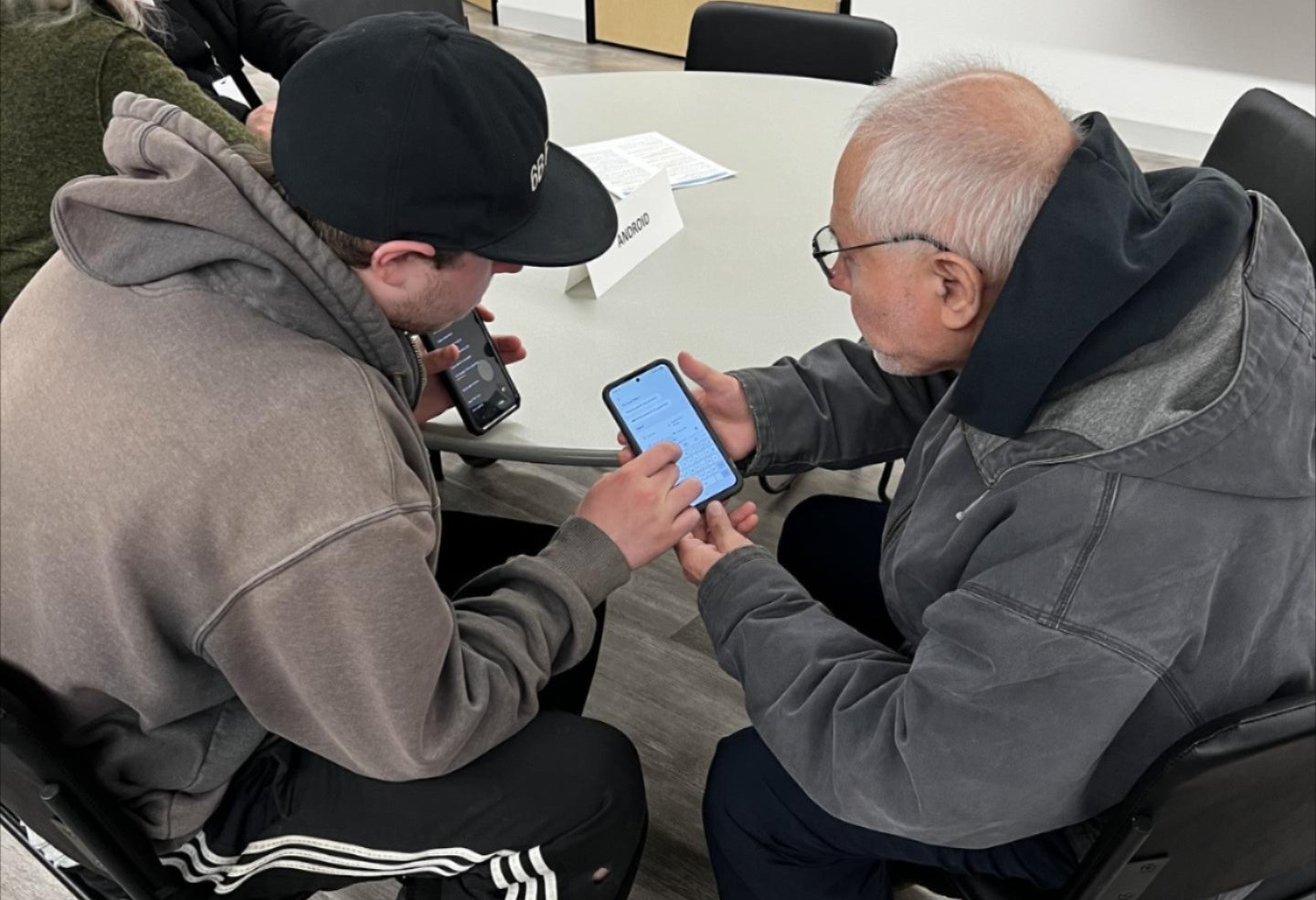 A student helps a senior citizen with his phone.