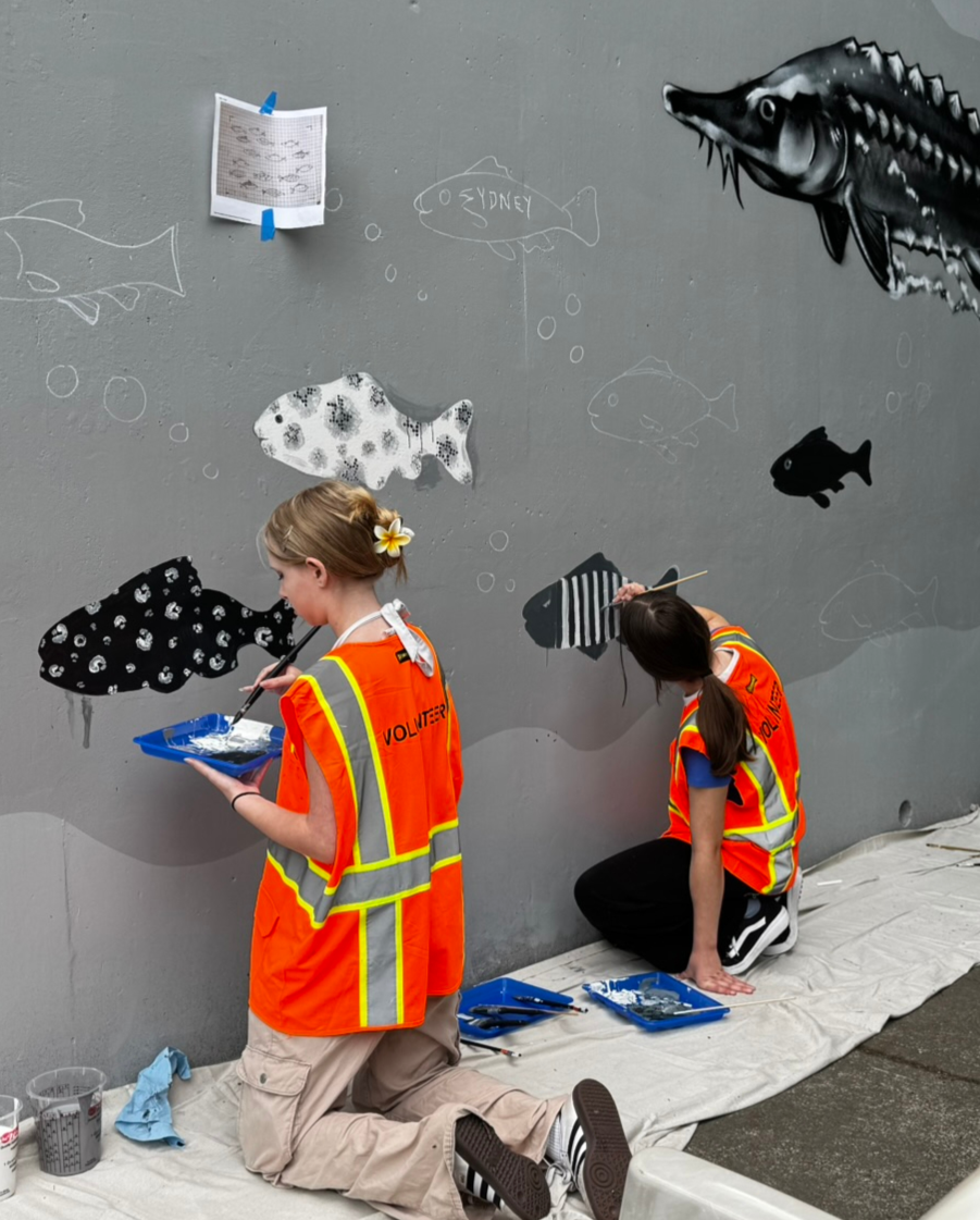 Two students paint fish on a new mural near Klineline Pond.