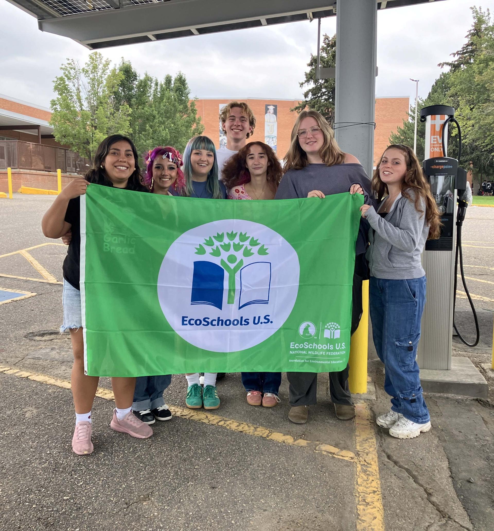 Students smile with an EcoSchools U.S. green flag in front of their school