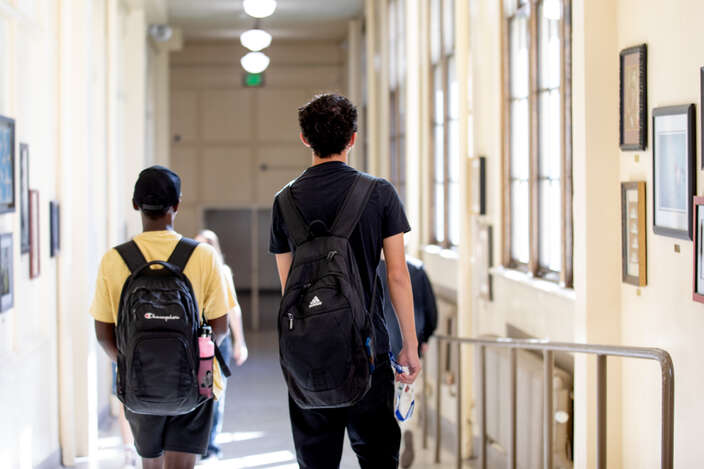Two high school students walk to class in the hallway of their school with backpacks on