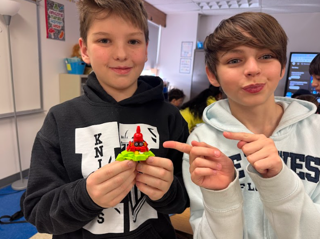 student points the the lego animal his friend is holding up for the carmera