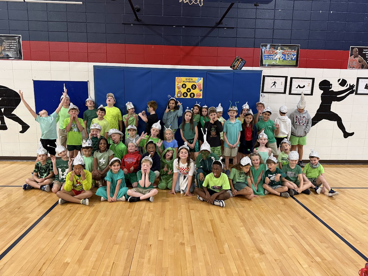 A group of children in green shirts and white hats pose for a photo in a gym.
