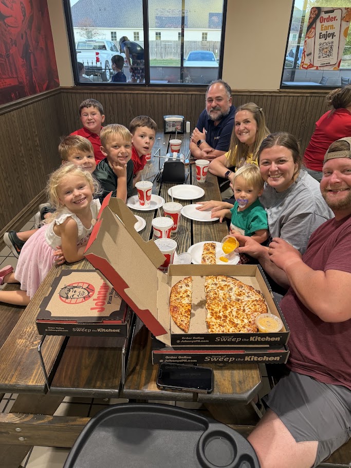 A family sits at a table in a restaurant, with two boxes of pizza in front of them.