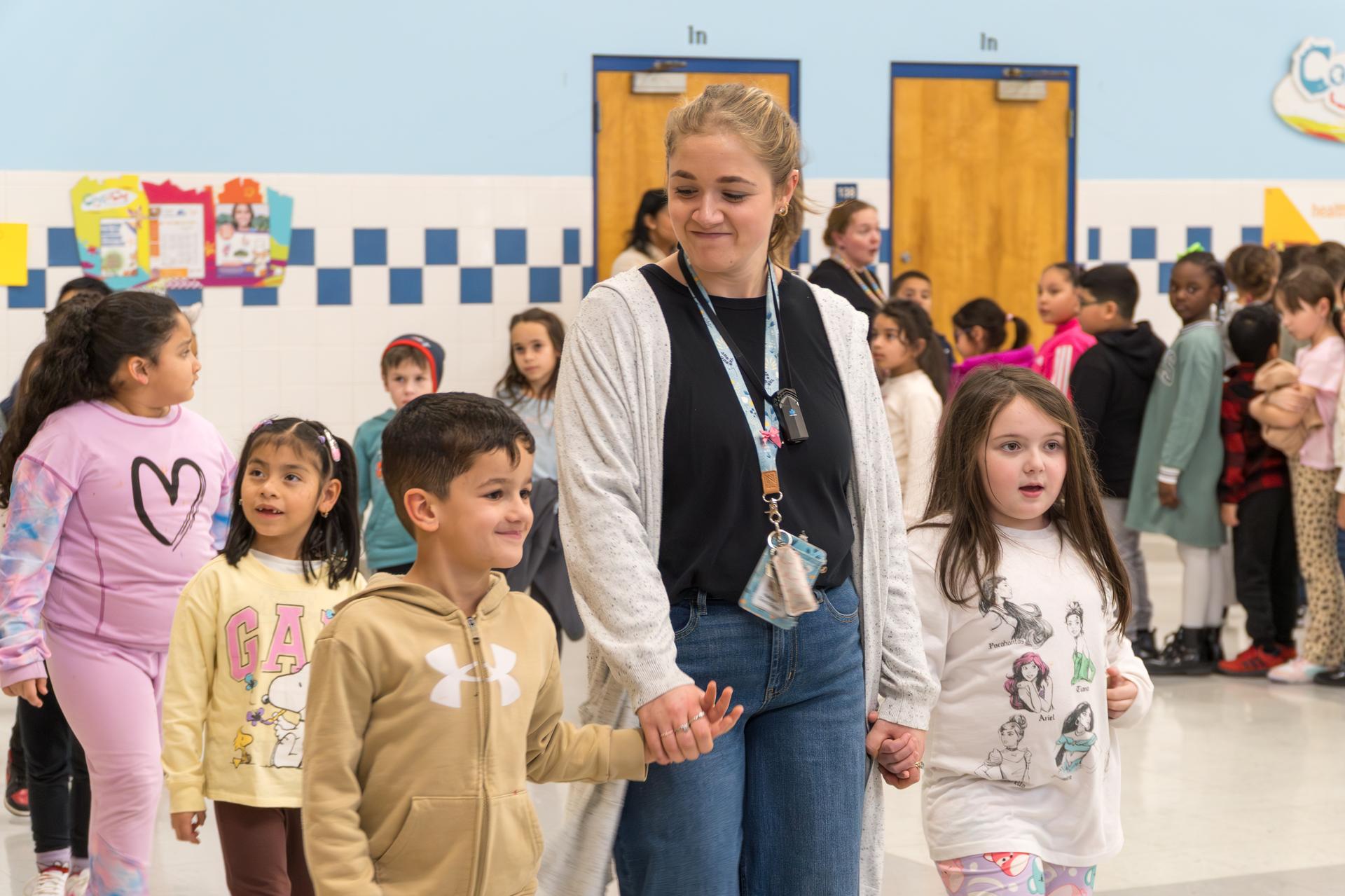 A teacher walks with two students, holding one of their hands on either side.