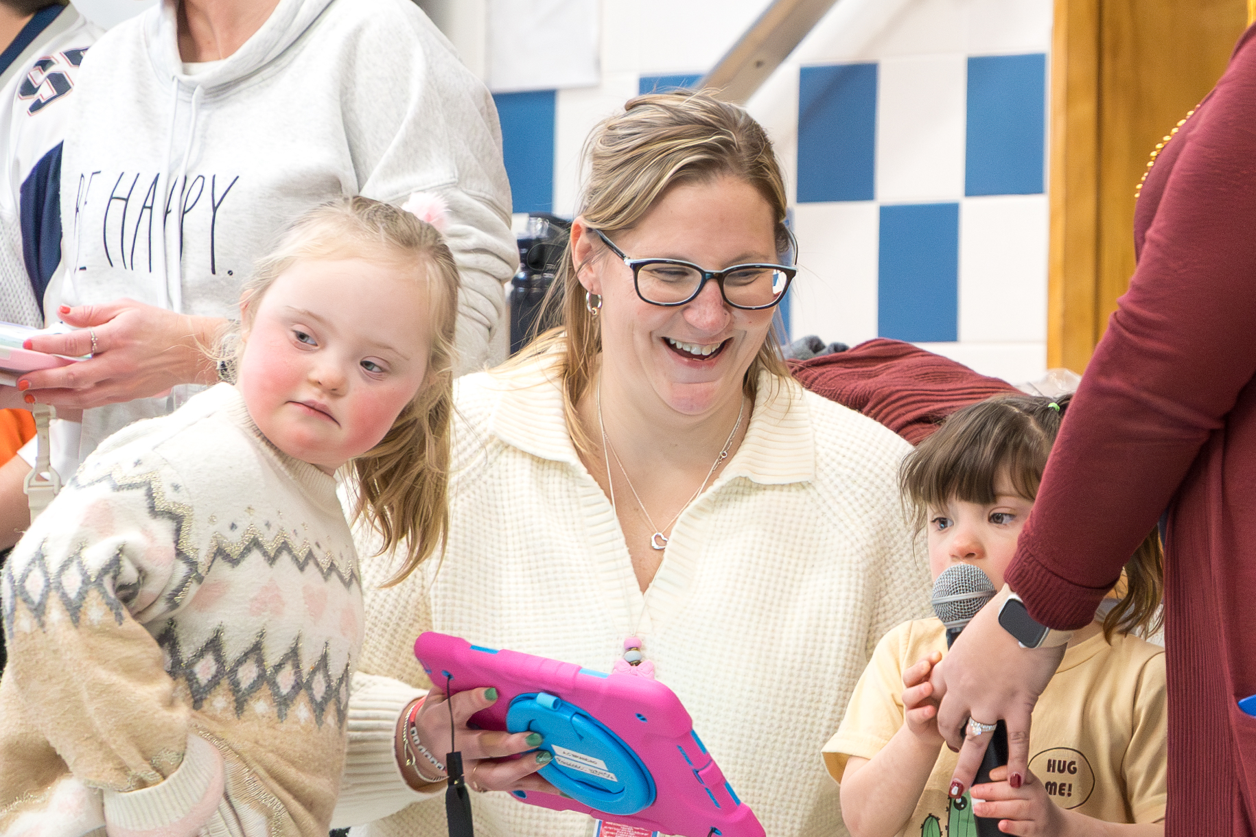 A Richer staff member kneels and holds up a tablet while smiling as a student speaks into a microphone.