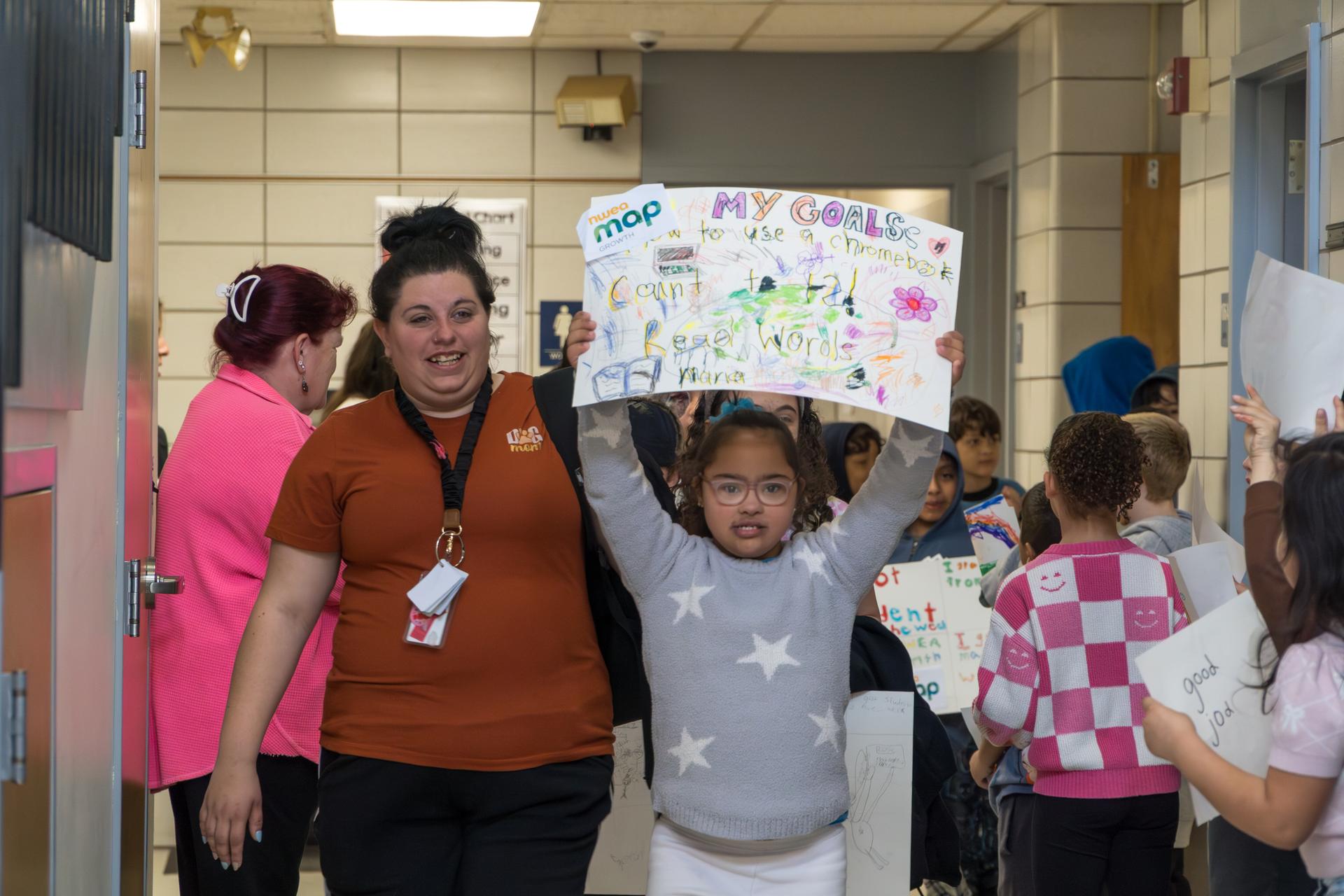 A Richer School student holds up their Growth Walk poster. A teacher walks besides the student.