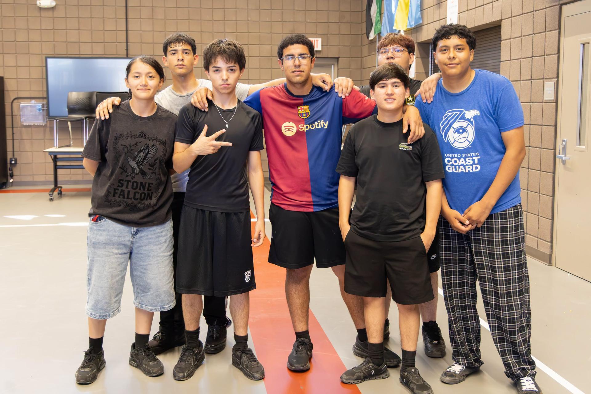 A group of young people, wearing various clothes, stand in a gymnasium and pose for a photograph.