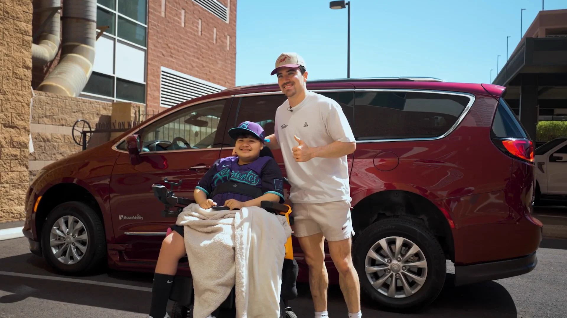 A man stands next to a red SUV, with a child in a wheelchair beside him.