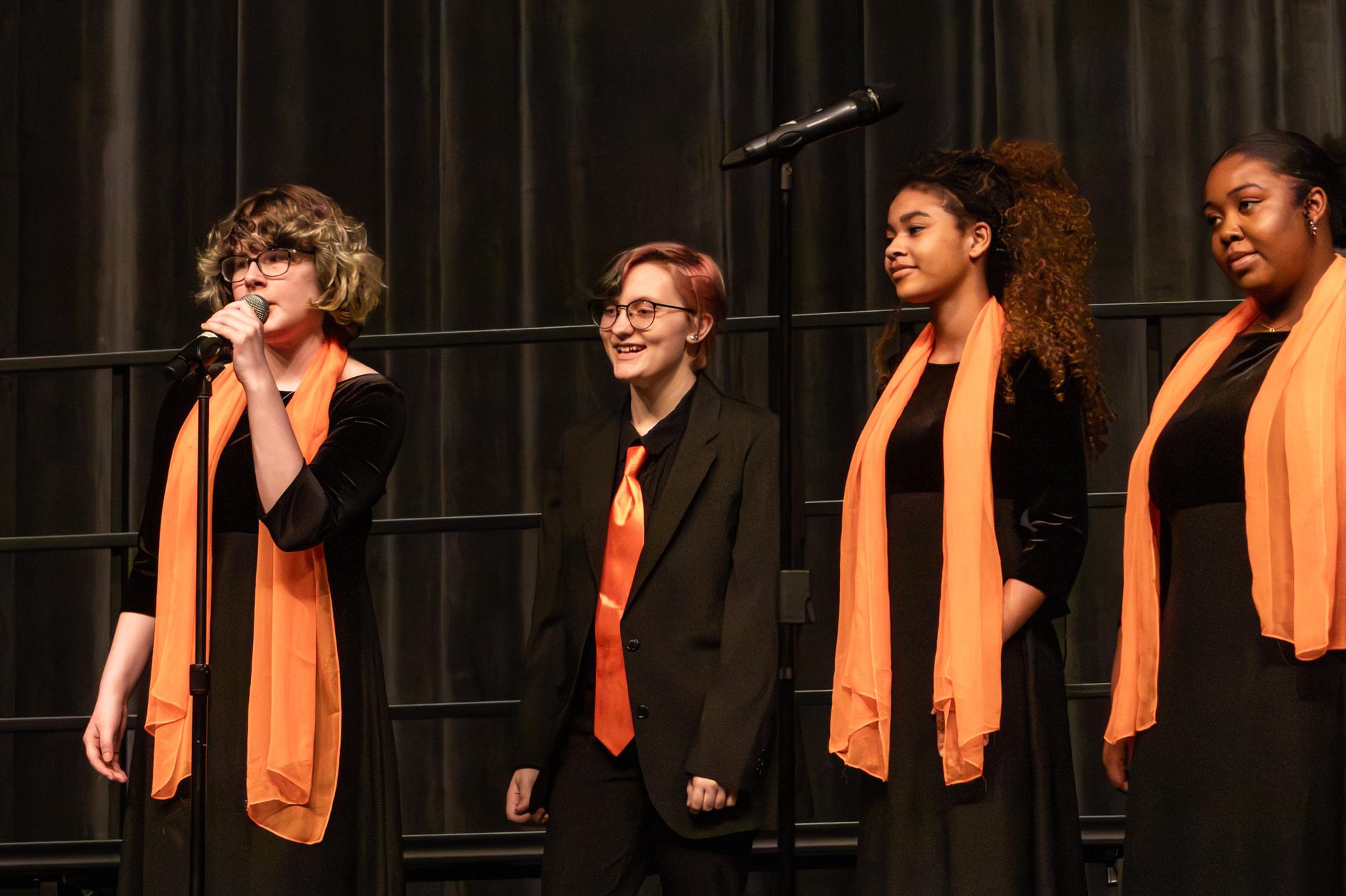 4 students in black and orange singing