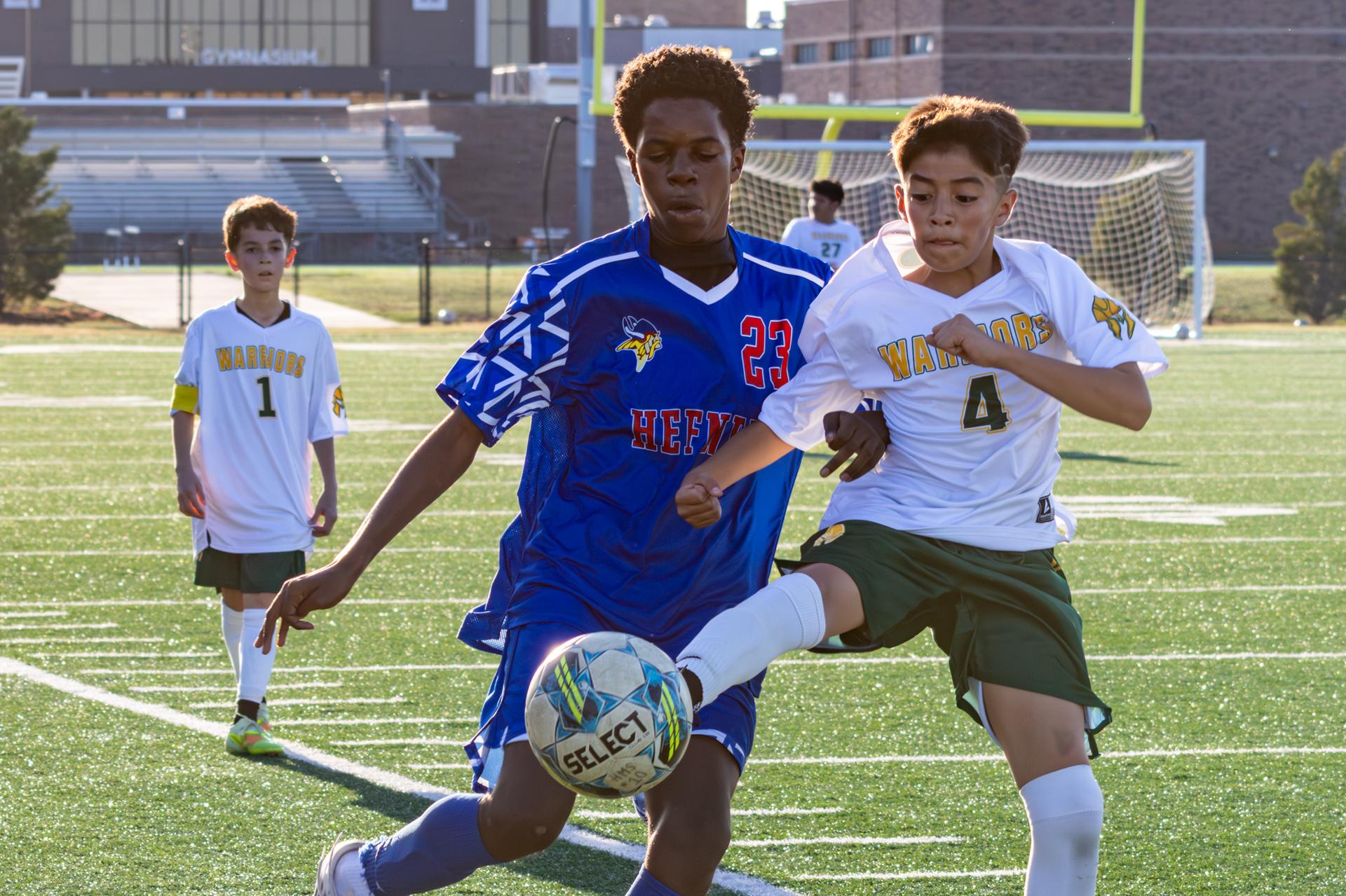 hefner athlete going for the ball with a western oak student kicking the ball