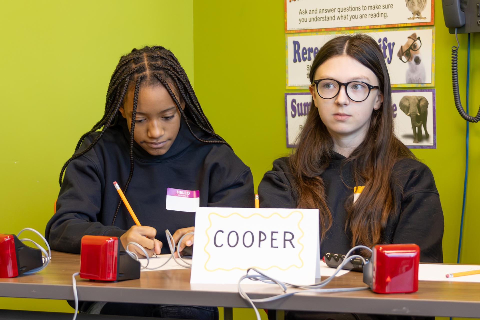 2 female students, one student is writing something down with a pencil