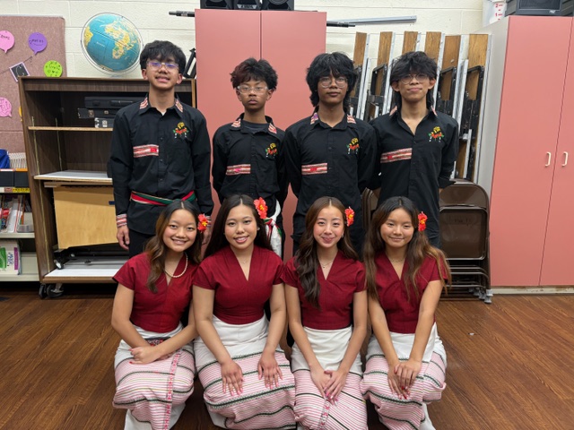4 male Burmese dancers standing in the back row, 4 female Burmese dancers kneeling in the front row.